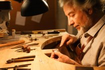 Профильное представление ориентированного зрелого мужчины ювелира, работающего с инструментами в мастерской — стоковое фото