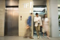 Размытые молодые бизнесмены, входящие и выходящие из лифта в современном офисе — стоковое фото