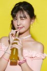 Bela jovem bebendo bebida refrescante e piscando na câmera no amarelo — Fotografia de Stock