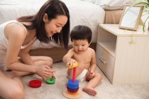 Щаслива молода мати дивиться на дитину, граючи з барвистою освітньою іграшкою вдома — стокове фото