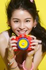 Bela elegante jovem asiático mulher segurando colorido câmera e sorrindo no amarelo — Fotografia de Stock