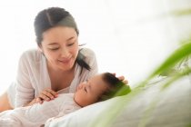 Happy young asian woman looking at her lovely baby sleeping on bed, selective focus — Stock Photo