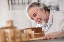 Close-up view of smiling professional mature architect working with building model at workplace — Stock Photo