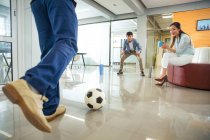 Cropped shot of young businessmen playing soccer and smiling businesswoman holding cup during break in office — Stock Photo