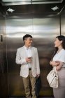 Happy young asian businessman and businesswoman smiling each other in elevator — Stock Photo