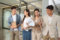 Sonriente joven asiático negocios colegas caminar y discutir los papeles en oficina - foto de stock