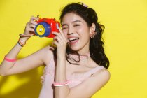 Atraente feliz jovem asiático mulher segurando colorido câmera e sorrindo no amarelo — Fotografia de Stock