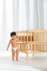 Adorable asian toddler child in diaper walking near crib at home, full length view — Stock Photo