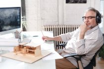 Профессиональный зрелый архитектор в наушниках, работающий с новым проектом и использующий настольный компьютер в офисе — стоковое фото