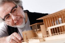 Крупный план концентрированного профессионального зрелого архитектора в очках, работающего со строительной моделью на рабочем месте — стоковое фото