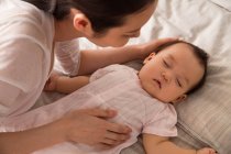 Plan recadré de jeune mère regardant bébé mignon dormir sur le lit — Photo de stock