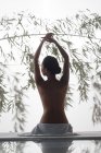 Rückansicht einer nackten jungen Frau, die auf einem Massagetisch sitzt und im Wellnessbereich die Hände hebt — Stockfoto