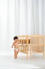 Adorable happy baby in diaper walking near crib in bedroom — Stock Photo