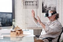 Усміхнений зрілий архітектор використовує гарнітуру віртуальної реальності на робочому місці — стокове фото