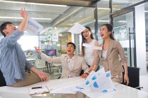 Схвильовані молоді азіатські бізнес-колеги кидають папери в сучасному офісі — стокове фото