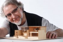 Arquitecto maduro profesional trabajando con el modelo de construcción y sonriendo a la cámara - foto de stock