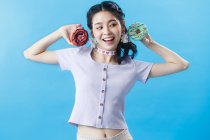 Beautiful happy young asian woman holding donuts isolated on blue background — Stock Photo