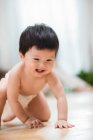 Очаровательный счастливый азиатский малыш в подгузнике ползает по полу дома — стоковое фото