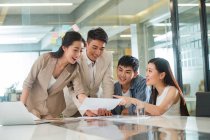 Усміхнені молоді азіатські бізнесмени і бізнесмени дивляться на папір і обговорюють проект в офісі — стокове фото