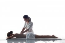 Вид сбоку красивой молодой азиатской женщины, получающей массаж на белом фоне — стоковое фото
