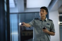 Junge asiatische Sicherheitsmann hält Taschenlampe und Walkie-Talkie im Büro in der Nacht — Stockfoto