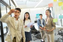 Blick durch das Glas junger asiatischer Geschäftsleute, die während eines Meetings im Büro Notizen machen — Stockfoto