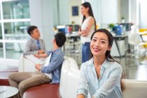 Beautiful happy young asian businesswoman smiling at camera in modern office — Stock Photo