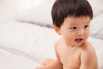 Porträt eines entzückenden asiatischen Babys, das auf dem Bett sitzt und wegschaut — Stockfoto