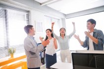 Счастливая молодая азиатская бизнес-команда празднует успех и дает друг другу пять в современном офисе — стоковое фото