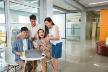 Glückliche junge asiatische Mitarbeiter, die während der Kaffeepause im Büro gemeinsam Tassen halten und Laptop benutzen — Stockfoto