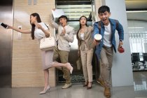 Young professional asian businesspeople running from elevator to workplace in office — Stock Photo