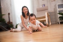 Ganzkörperansicht einer glücklichen jungen Mutter, die ihr auf dem Boden kriechendes Baby betrachtet — Stockfoto