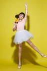Longitud completa vista de hermosa chica asiática feliz en falda celebración colorido piruleta y sonriendo a la cámara sobre fondo amarillo - foto de stock