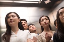 Vista basso angolo di gravi giovani asiatici in piedi insieme in ascensore — Foto stock