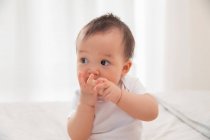 Hermosa asiático bebé comiendo pedazo de pelado fruta y mirando lejos en casa - foto de stock