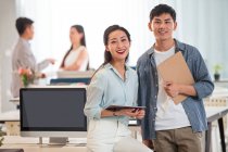Happy young asian and businesswoman holding clipboard and digital tablet, standing together and smiling at camera in office — Stock Photo