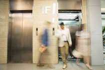 Размытые молодые бизнесмены, входящие и выходящие из лифта в современном офисе — стоковое фото