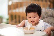 Милий усміхнений малюк сидить і дивиться на їжу в мисці вдома — стокове фото