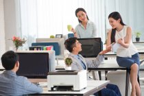 Bello asiatico uomo d'affari parlando con sorridente femmina colleghi in moderno ufficio — Foto stock