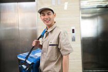 Guapo joven asiático entrega hombre con bolsa sonriendo a cámara en oficina - foto de stock