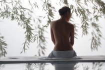 Rückseite der attraktiven nackten Frau sitzt auf Massagetisch im Wellnessbereich — Stockfoto