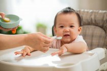 Plan recadré de mère tenant cuillère et nourrissant adorable bébé asiatique — Photo de stock