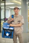 Handsome young asian courier with bag smiling at camera in office — Stock Photo