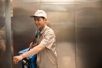 Sorrindo jovem asiático entrega homem com saco de pé no elevador — Fotografia de Stock