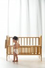 Вид сбоку восхитительного малыша в пеленке, идущего рядом с кроваткой, вид в полный рост — стоковое фото