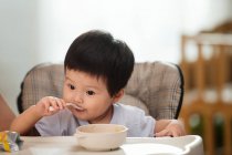 Cute asian toddler holding spoon and eating at home — Stock Photo