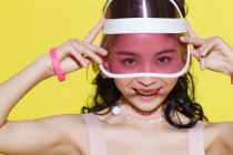 Красива щаслива азіатська дівчина регулює шапку і посміхається на камеру ізольовано на жовтому — стокове фото