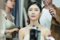 Recortado disparo de estilistas sosteniendo herramientas y haciendo peinado a hermosa joven asiática mujer en salón de belleza - foto de stock