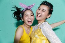 Красиві щасливі стильні азіатські подружки розважаються і танцюють на синьому фоні з барвистим конфетті — стокове фото