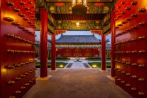 Vista attraverso i cancelli a bella architettura tradizionale asiatica con colonne rosse e piante verdi in cortile — Foto stock